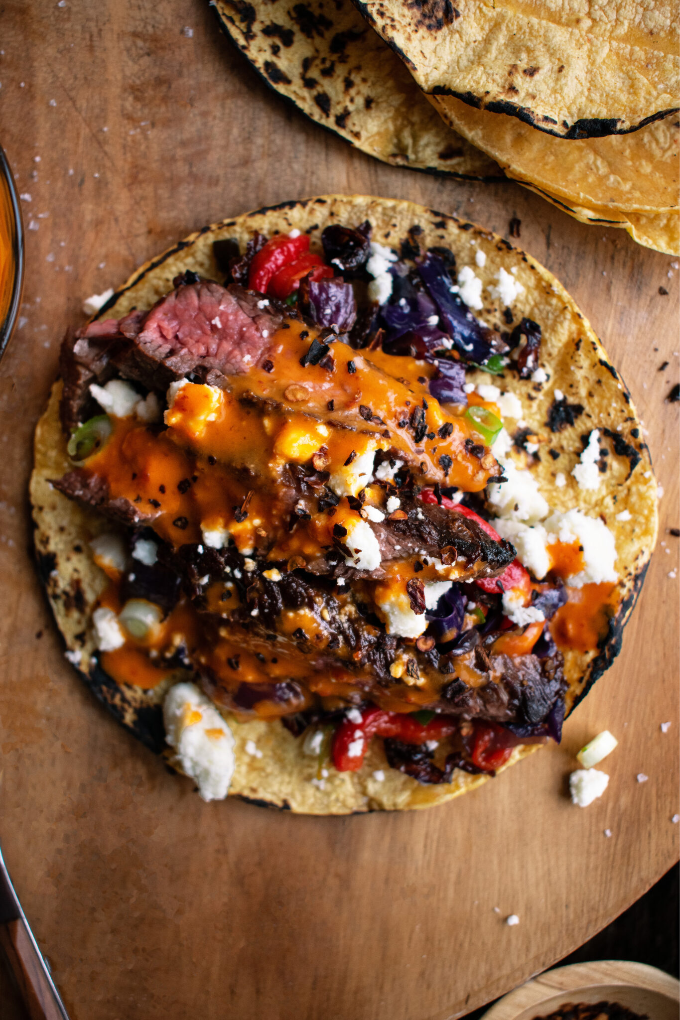 Open-fire sliced skirt steak over a charred corn tortilla with fire-roasted peppers, cabbage, queso fresco, and red salsa — The Asado.