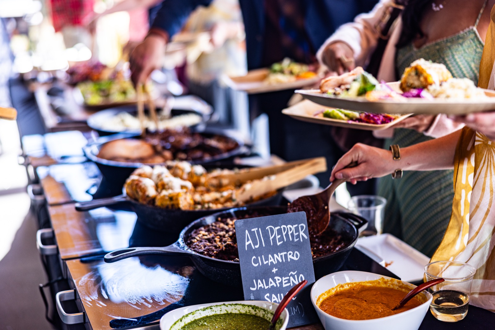 Guests serving themselves along a Net Zero Ranch buffet line of cast-iron skillets and house sauces.