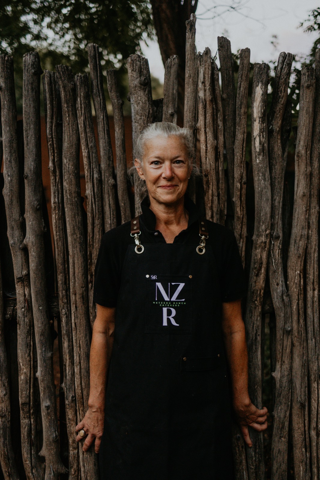 A Net Zero Ranch crew member in the NZR apron, portrait against a coyote-fence backdrop.