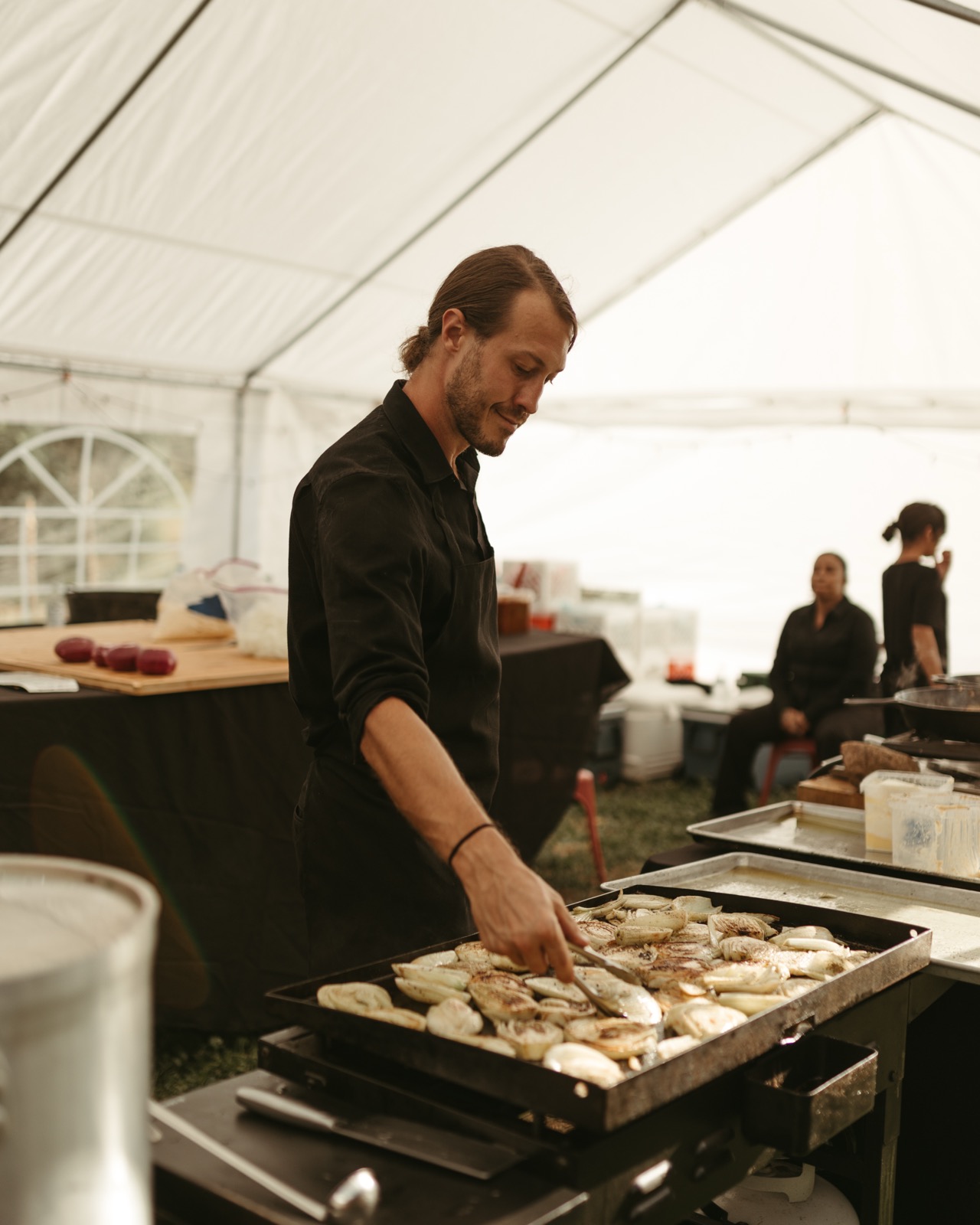 A Net Zero Ranch chef searing vegetables on the plancha under the event tent.