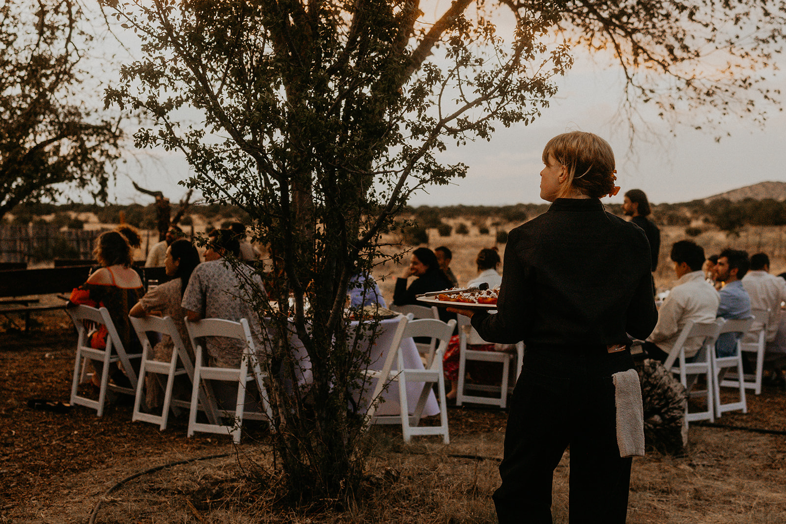 A Net Zero Ranch server carrying a plated course to the tables at dusk.