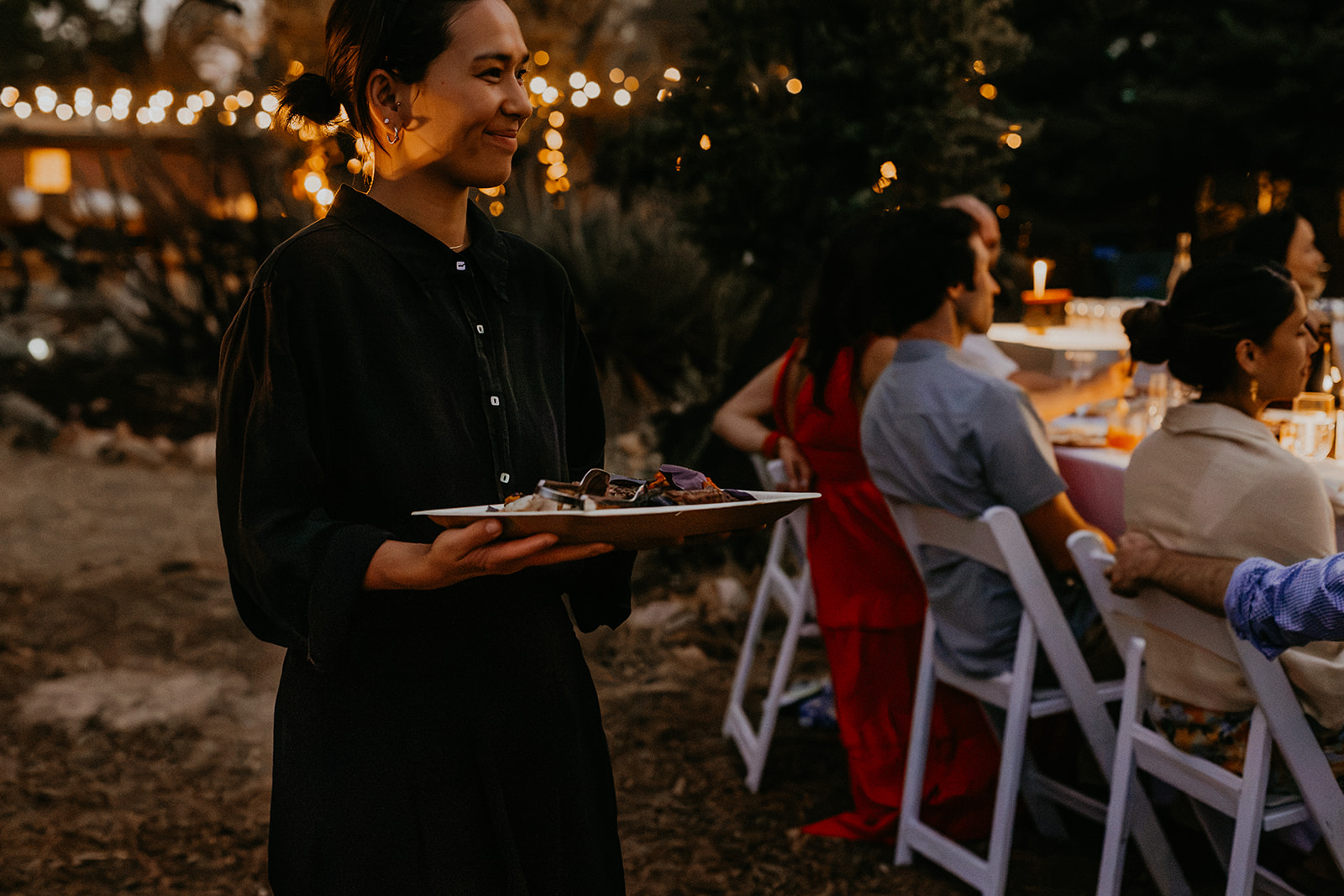 A Net Zero Ranch server with a plated dish under string lights.