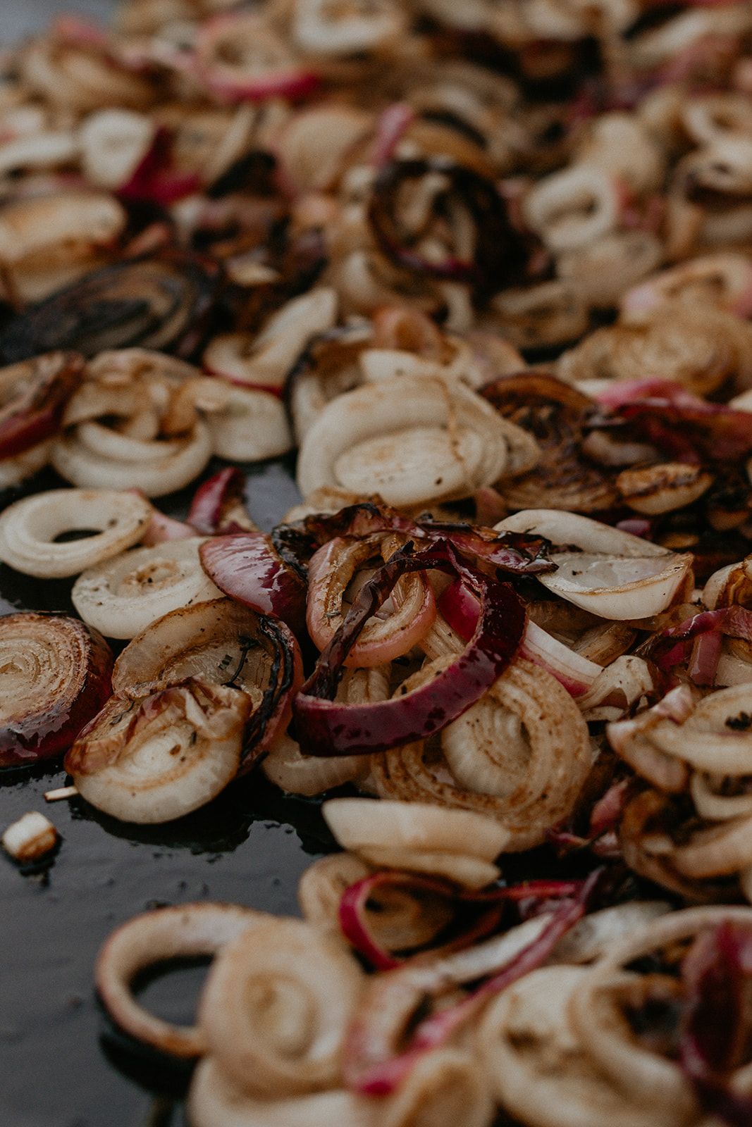 Sliced red and white onions charring on the plancha — The Asado table.