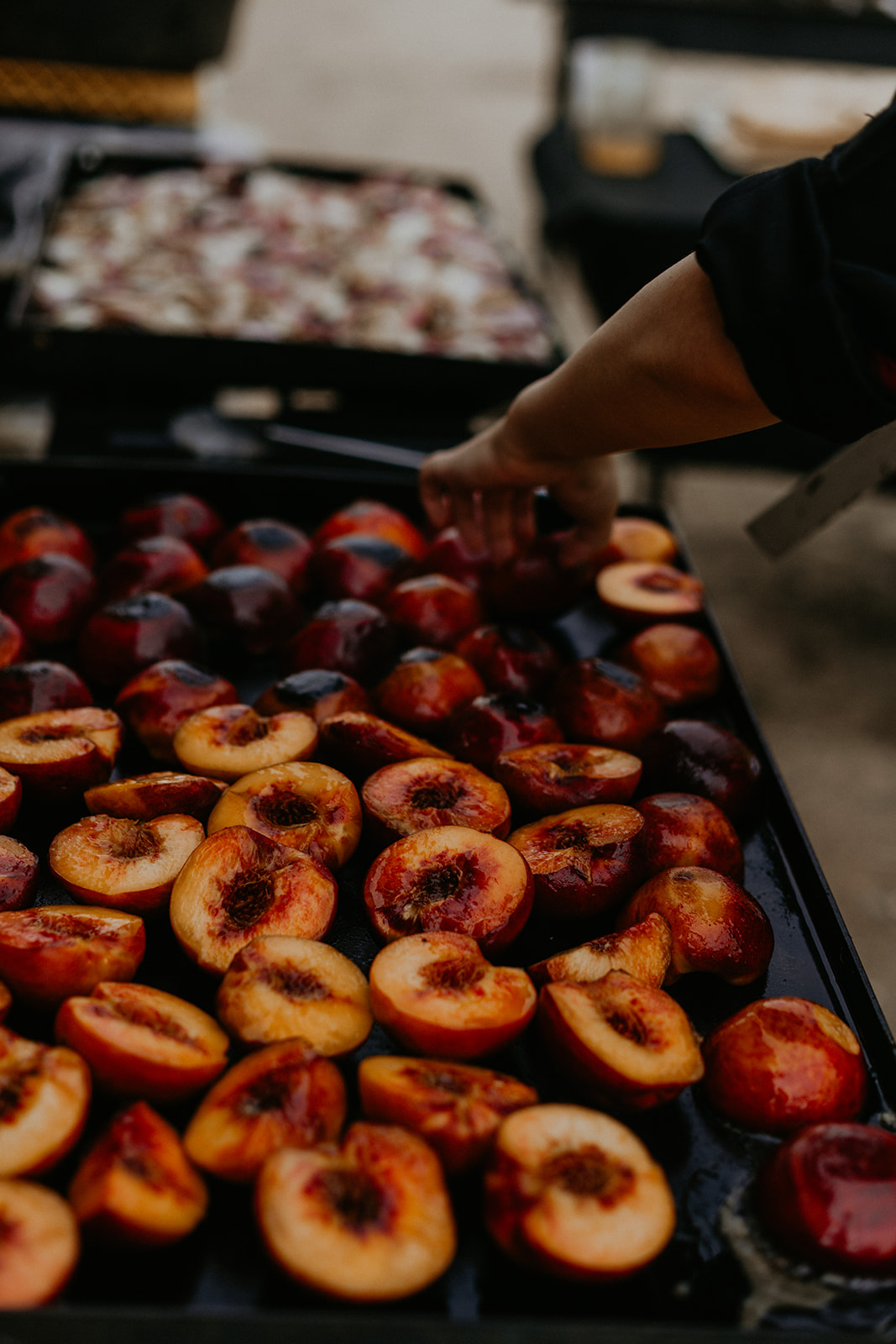 A full tray of halved peaches grilling on the plancha — The Asado table.