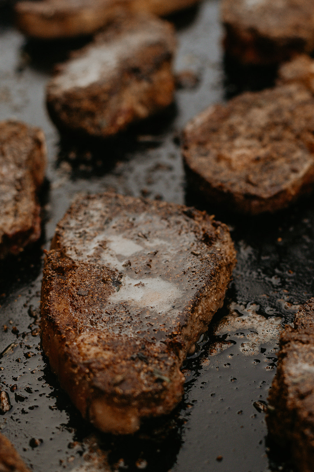 Spice-crusted bison ribeyes searing with butter on the plancha — The Asado table.