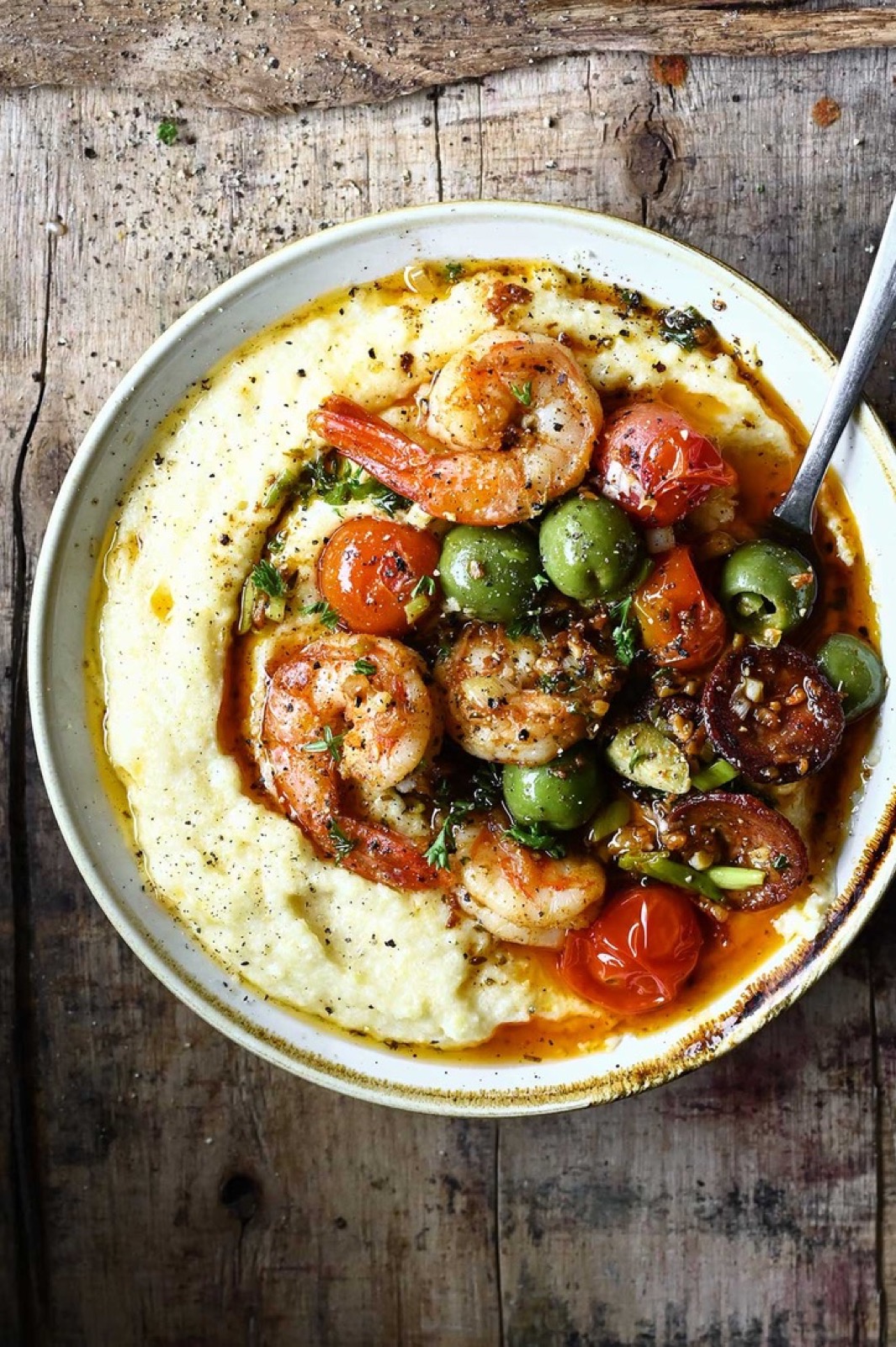 Creamy polenta topped with grilled shrimp, blistered tomatoes and olives — The Asado table, with or without shrimp.
