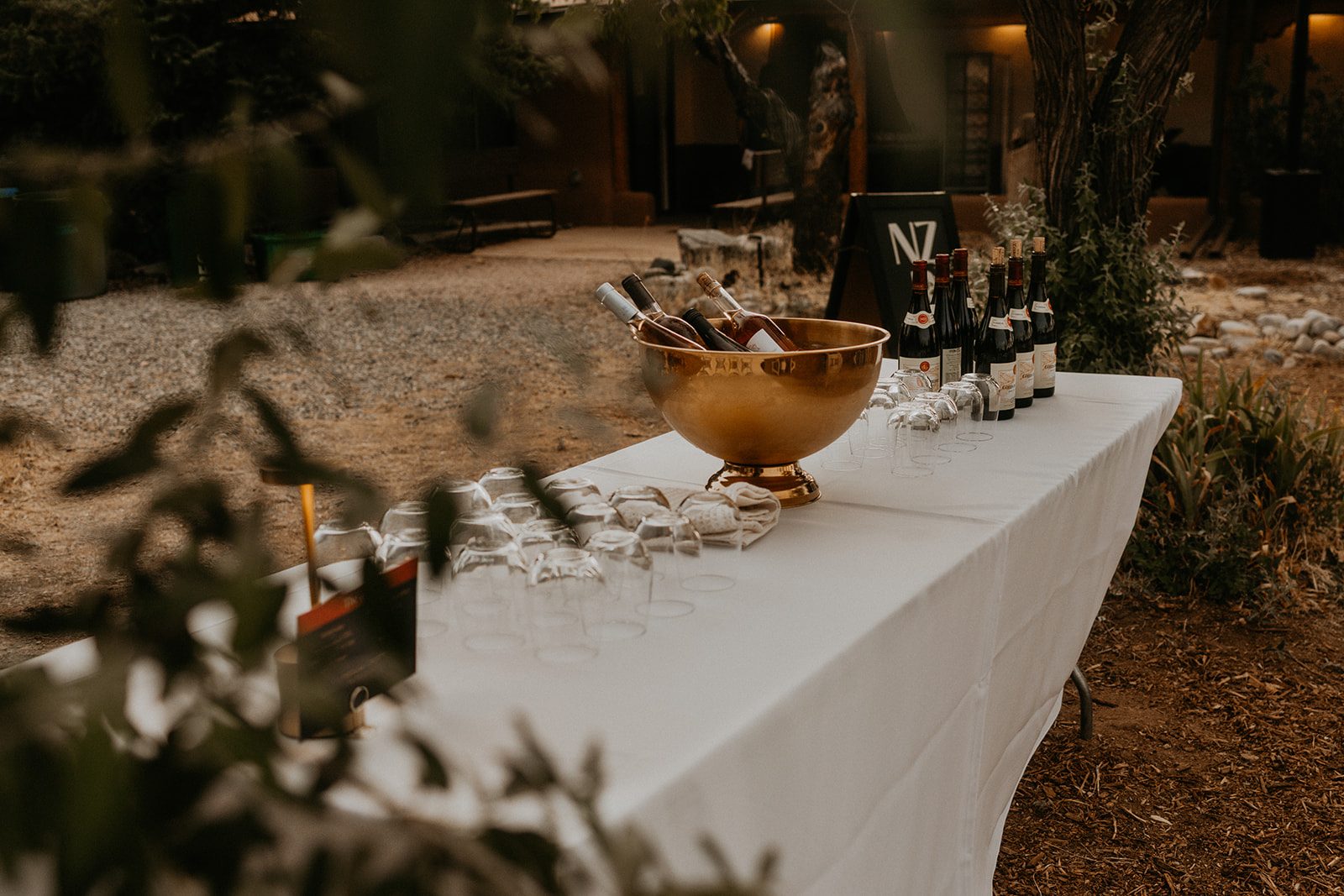 The Wine Table at a Net Zero Ranch wedding — bottles chilling in a gold bowl on ice, glasses set out, more wine beside the Net Zero Ranch sign.