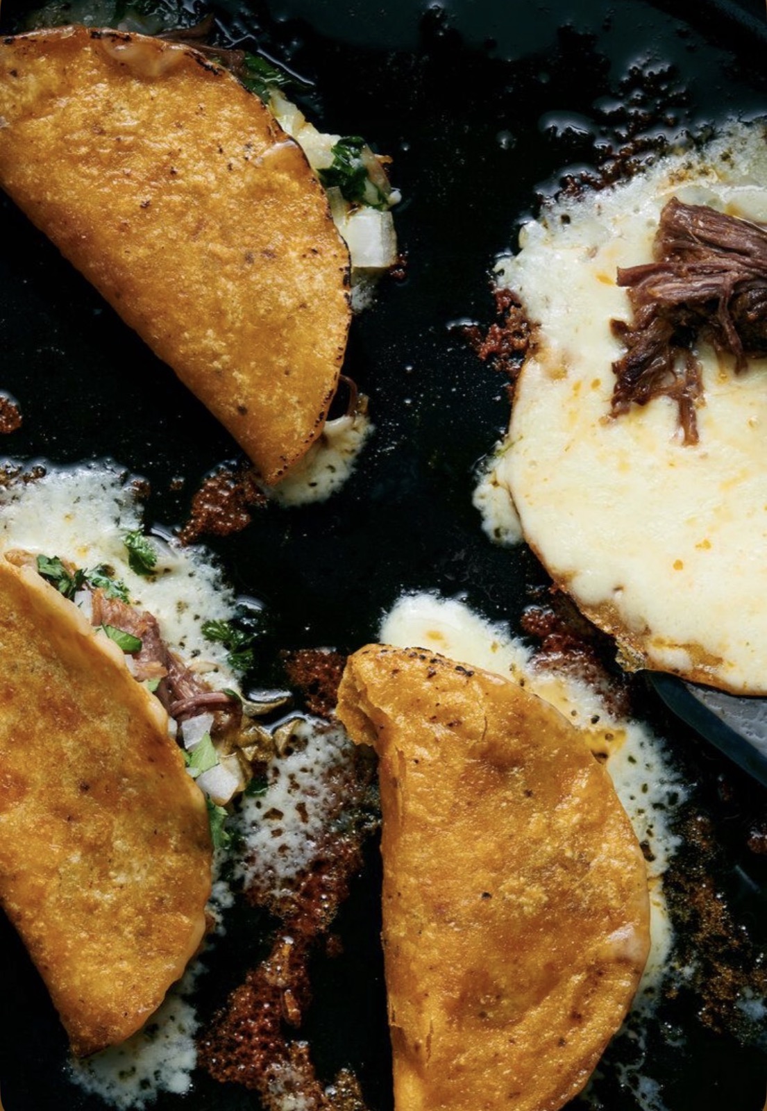 Crispy quesabirria tacos with melted cheese and consommé in the skillet — The Charro table.