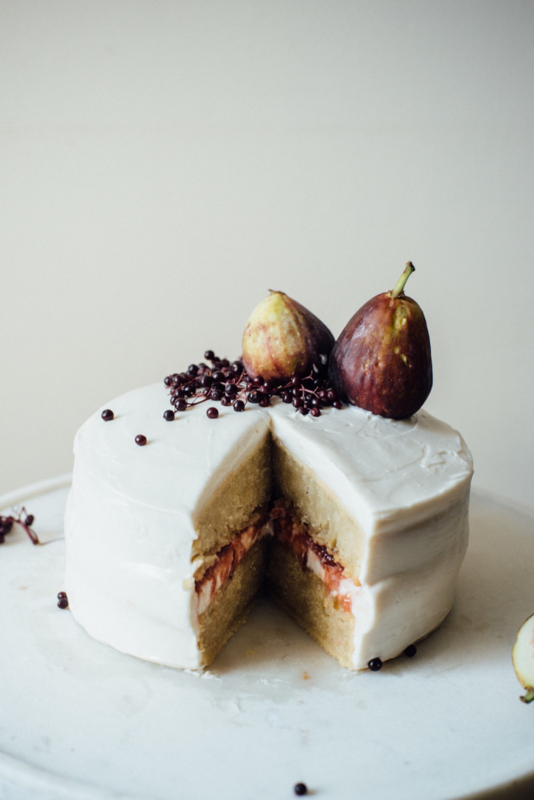 A white-frosted layer cake topped with fresh figs and elderberries — dessert station.