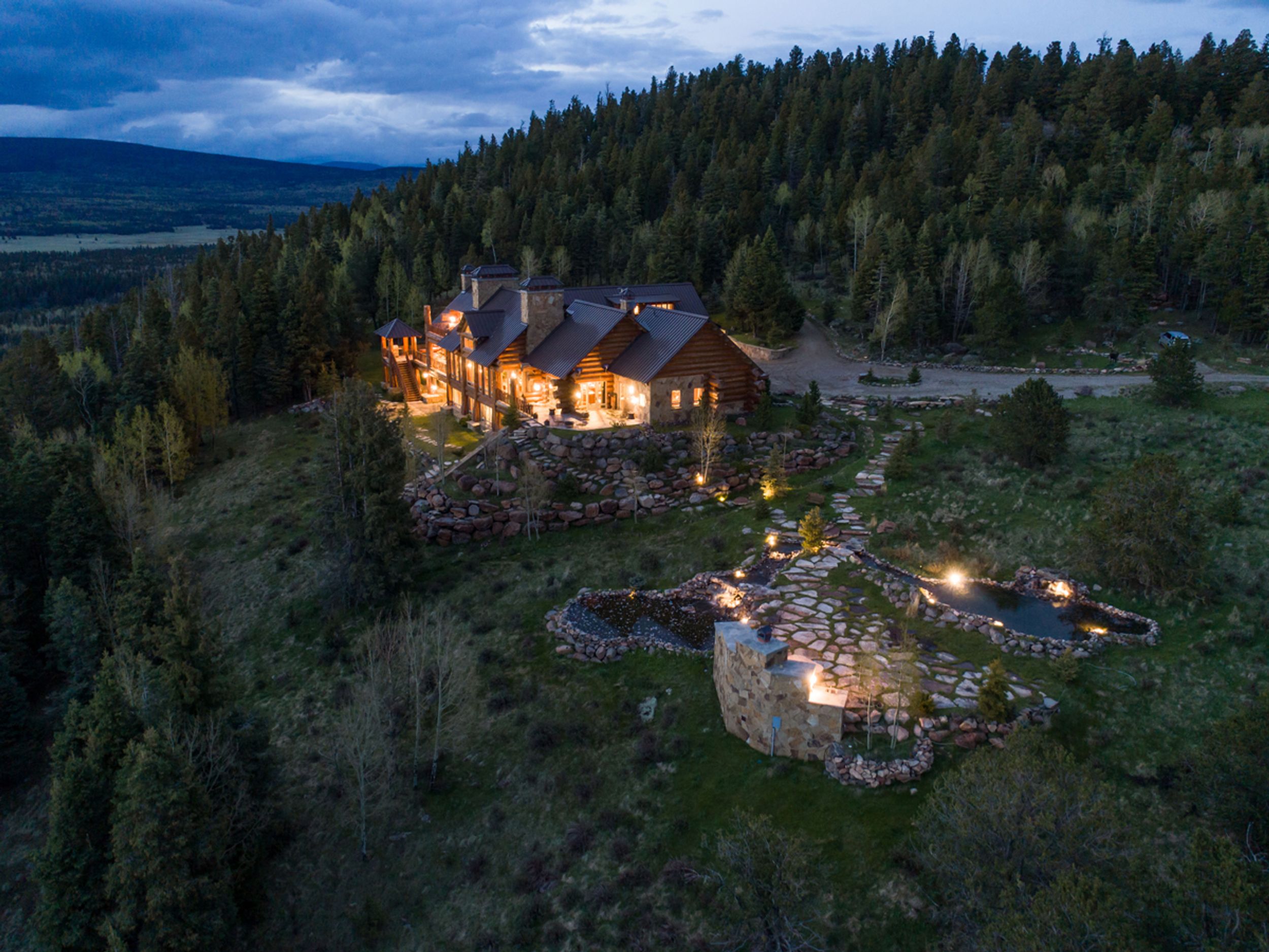 Los Cielos Ranch — log lodge at twilight on a high meadow above Angel Fire, NM, with stone pathways, fire pits, and ponds.